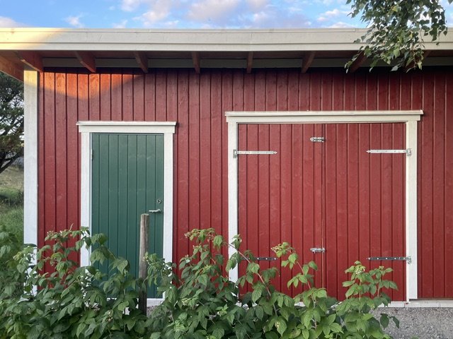 Redskapsboden rakt framifrån med grön enkeldörr och röd dubbeldörr